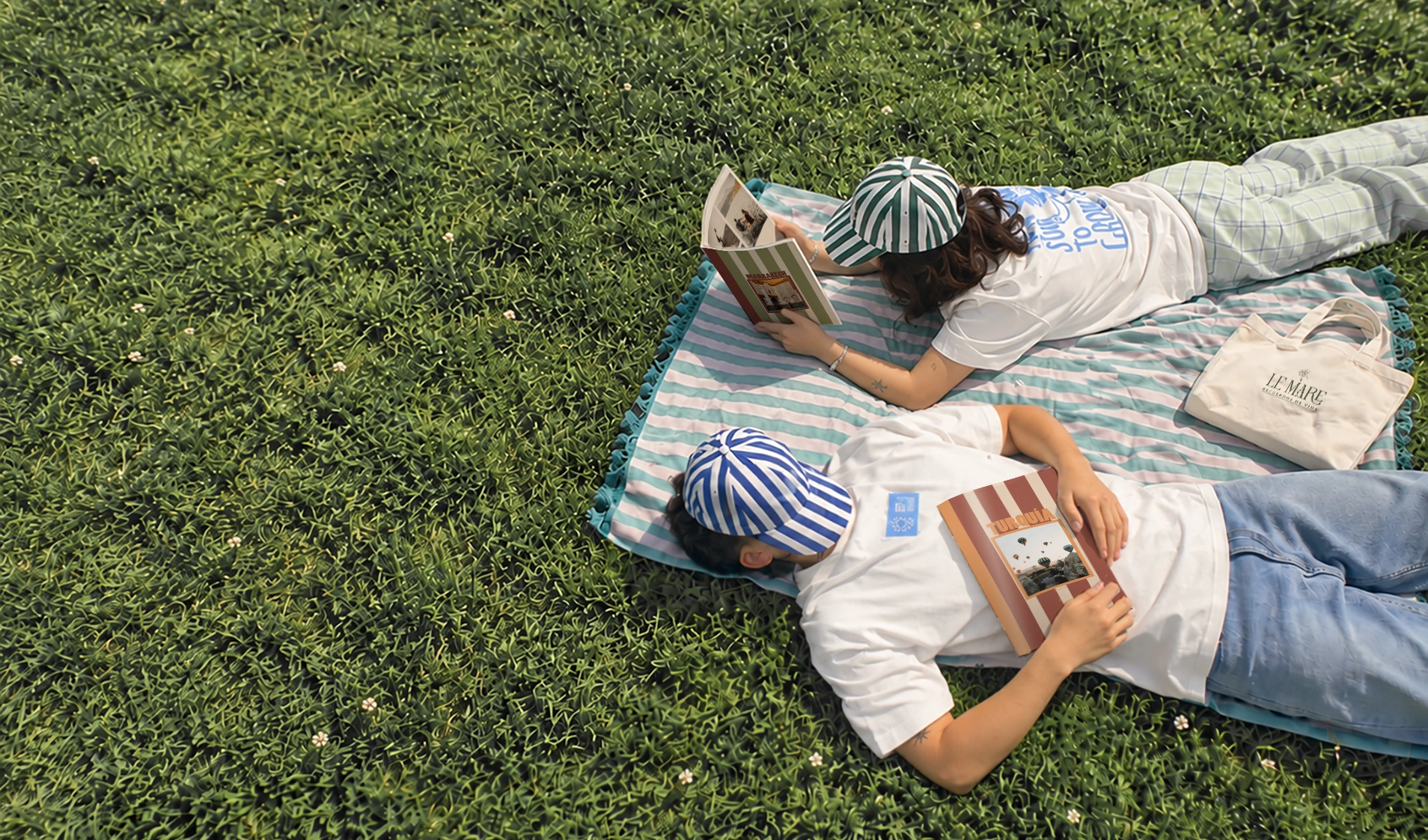 Dos personas leyendo álbumes Le Mare sobre una manta en el césped